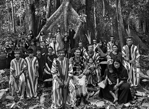 Group of about thirty native Amazonian people in front of a massive tree in the forest.