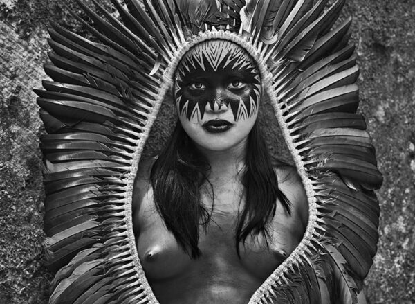Upper body close up of a naked woman wearing feather headdress.