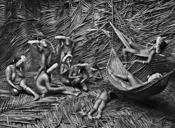 10 Naked women wearing headdresses in a room covered with palm leaves.