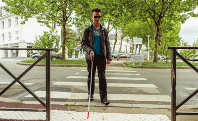 A man with a white cane crosses the street.