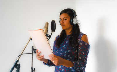 Woman in front of a microphone reads a text in a recording studio.